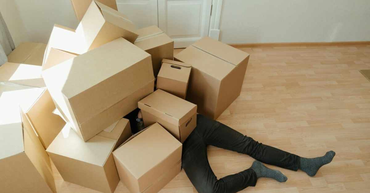 Das Bild zeigt eine Person, die unter einem Haufen Kartons liegt